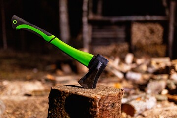 Axe with a strong plastic handle is stuck in a wooden stump against a background of chopped wood....