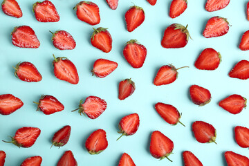 Halves of delicious ripe strawberries on light blue background, flat lay