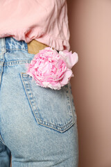 Woman with pink peony bud in pocket on beige background, closeup