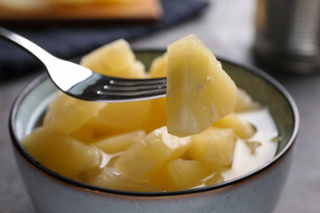Fork with canned pineapple piece over bowl on table, closeup