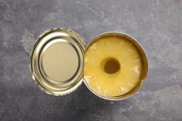 Tin with canned pineapple on grey table, top view