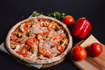 Tasty italian pizza and cooking ingredients tomatoes, herb, cheese on black concrete background. Hot pancetta pizza.