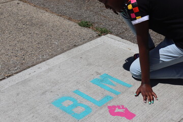 Child kneeling near BLM Black Lives Matter words on Sidewalk