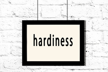 Black frame hanging on white brick wall with inscription hardiness