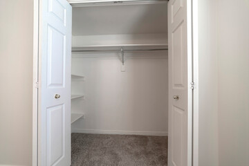 Walk in closet with double hinged doors plain white wall and gray floor carpet