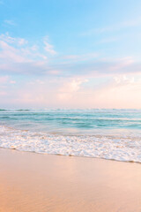 Sandy beach, blue cloudy sky and soft ocean wave with warm sunset light.