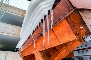 Icicles at the edge of corrugated metal roof with mound of fresh snow in winter