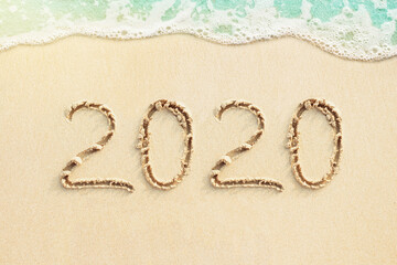Numbers  2020 handwritten on the beach and soft blue ocean wave on background