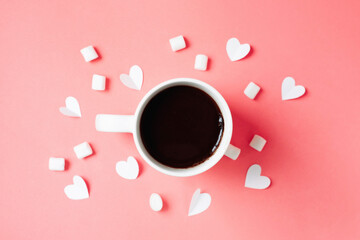 Cup of dark coffee, paper hearts and marshmallows on bright pink background with space for text