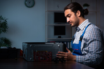 Young male technician repairing computer in workshop at night
