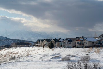 Fototapeta na wymiar Homes on snowy terrain ovelooking Wasatch Mountain peak and dark overcast sky