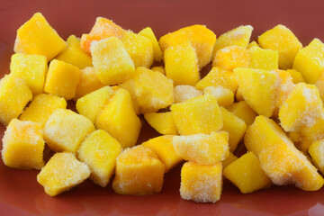 Closeup of frozen mango fruit chunk cubes with ice crystals on red plate