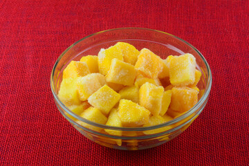 Frozen mango fruit chunk cubes with ice crystals in glass ingredient bowl on red tablecloth