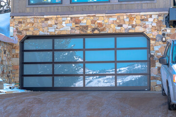 Garage door with glass panes reflecting a snowy hill landscape under blue sky