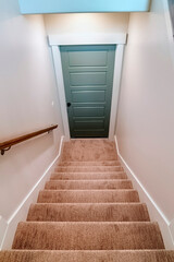 Indoor stairs of home with carpeted treads that leads down to the basement door
