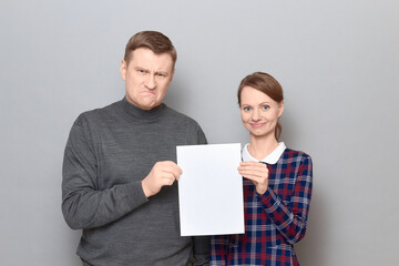 Portrait of adult couple holding together white blank paper sheet
