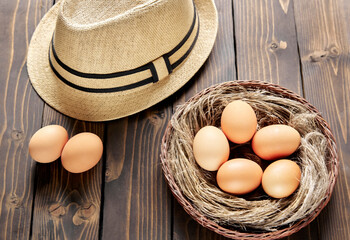 Nest in wicker basket with chicken eggs on a wooden table.