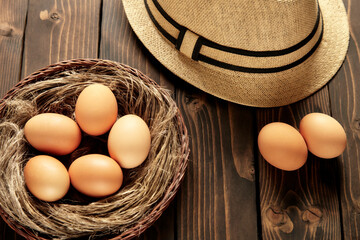 Nest in wicker basket with chicken eggs on a wooden table.