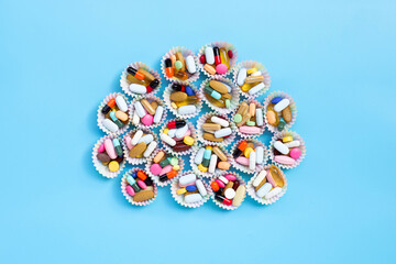 Fototapeta na wymiar Colorful tablets with capsules and pills in cupcake wrappers on blue background.