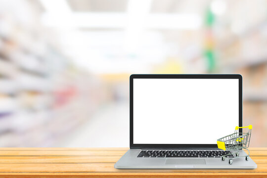 Shopping Online Concept : Yellow shopping cart put on laptop with blank white screen and blurry image in background.