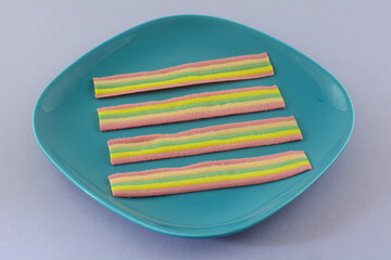 Chewy rainbow candy strips on blue dessert plate on lavender background