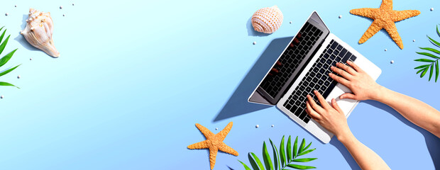 Person using a laptop computer with summer theme objects - flat lay