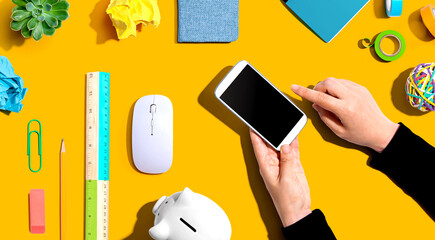 Office supplies with person using a smartphone - flat lay