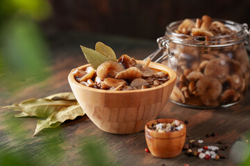 Homemade pickled honey agarics in wooden bowi and  open glass jar, spices, spoon, napkin,  on  wooden table. Marinated mushrooms are valuable source of protein. Fermented healthy food.