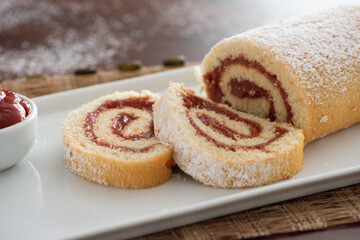 delicious roll cake with guava cream jelly and sugar sliced on white platter and blurred background