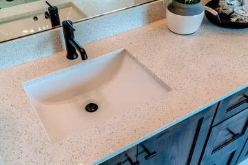 Single basin undermount sink with black faucet on white countertop over cabinet