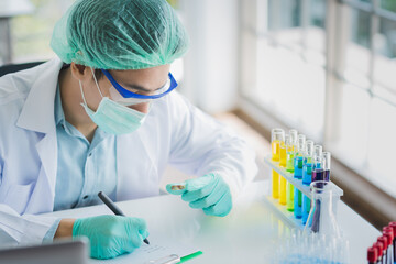 Professional Asian scientist or researcher man in work coat uniform examine liquid sample and record result detail in science lab