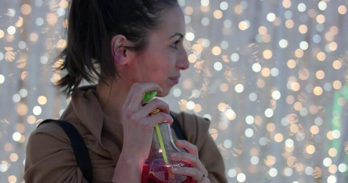 Young woman sipping from bendy straw at light show - bokeh background