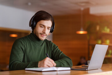 Concentrated guy with headset studying online, using laptop