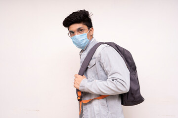 Young handsome asian boy ready for his college,wearing a mask, bag on his back, looking into the camera.