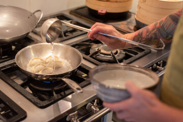 chef preparing asian gyoza on oven and pan with water