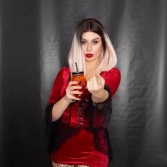 Blonde woman in vapmire dress hold orange glass in the shape of a skull in her hands