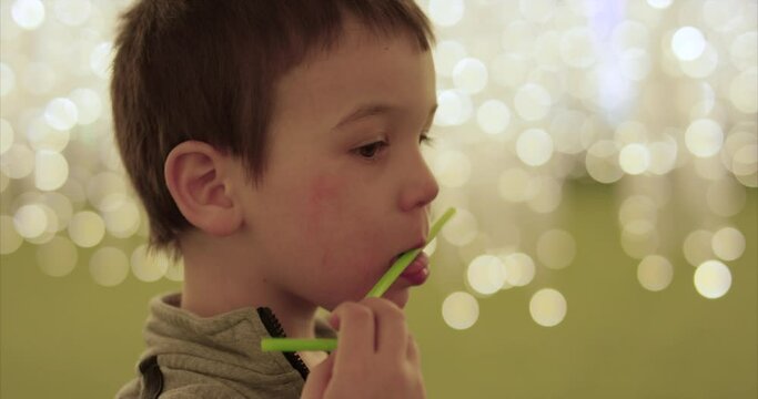 Toddler boy licking bendy straw in front of brightly lit background