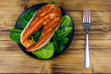 Grilled salmon steak with spinach on wooden table. Top view