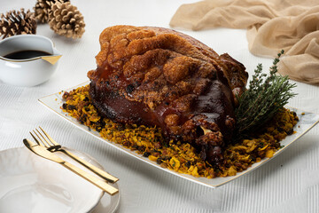 roasted pork shoulder ham meat on a white platter with dishes napkin and pines