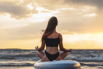 Young sexy woman surfer meditating on her sup board on the sunset. Mental health concept
