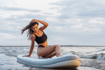 Fototapeta na wymiar Young sexy woman surfer sitting on her sup board. Rest at nature concept