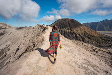 Young Asian woman walking on narrow crater ridge of Bromo volcano mountain, East Java island in Indonesia