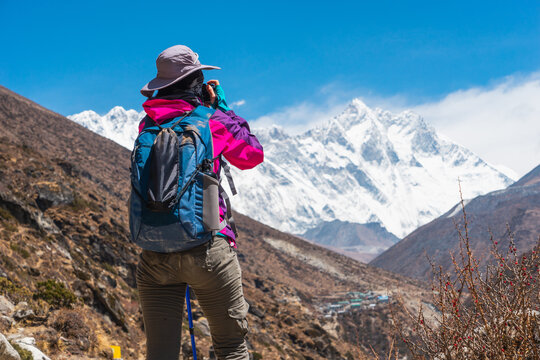 Young woman trekker taking picture while trekking in Everest Base Camp, Himalaya mountains range in Nepal