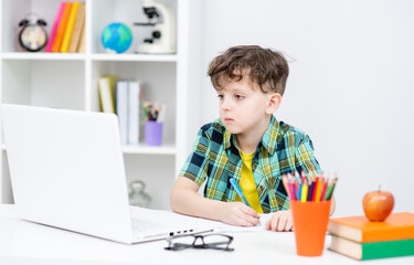 Young boy is doing homework and writing to notebook at home. Distance learning concept