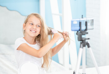 Young fashionable girl combs hair while recording a video for her followers on social networks. Kids blogger concept