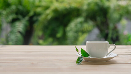 cup of tea with fresh tea leaves on wooden table with green nature blurred background