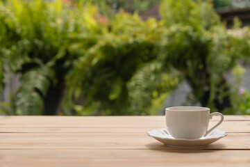 cup of coffee on wooden table with green nature blurred background