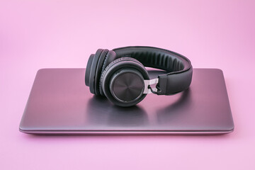 Closed laptop and earphones. Metallic notebook and black portable headphones on a pink background....