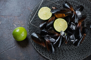 Raw iced mussels and limes on a metal fishing pond, elevated view on a dark brown stone background, studio shot