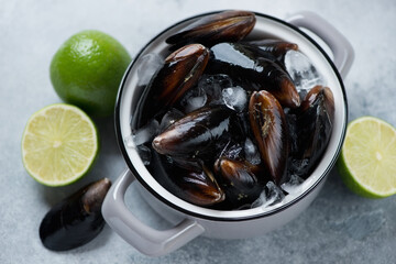 Grey pan with raw fresh iced mussels and limes over light-blue stone surface, horizontal shot, selective focus